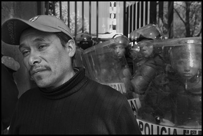 Un impresionante maestro de Michoacán se manifiesta en la Ciudad de México frente a una línea de policías. Profesores canadienses y estadounidenses de la Coalición Trinacional en Defensa de la Educación Pública se han organizado para defender la educación pública y apoyar los esfuerzos de maestros mexicanos para echar abajo las propuestas impulsadas por la USAID y fundaciones privadas, para introducir pruebas estandarizadas, eliminar protecciones de trabajo y promover una reforma corporativa de la educación. (David Bacon)