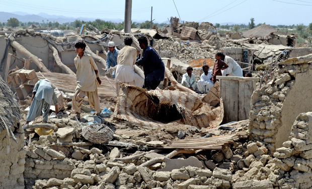 Pakistani villagers look for belongings amid the rubble of their dest